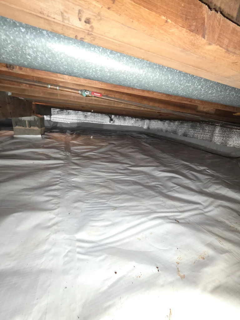 A clean crawl space with a shiny, reflective floor lining and wooden beams above. A metallic pipe runs along the ceiling, creating a tidy, organized feel.