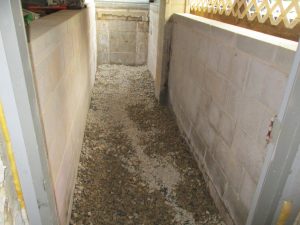 Basement area with gravel flooring and cinder block walls, illustrating foundation waterproofing and drainage solutions for preventing hydrostatic pressure damage in homes.