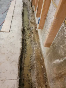 French drain trench installation along a basement wall during a waterproofing project in Morrisville, PA.